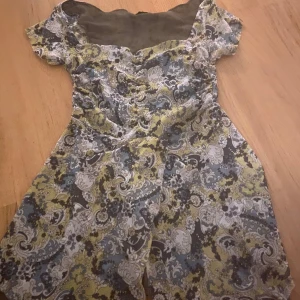 Mönstrad kortklänning från Eve - Kortklänning från Eve med unikt paisleymönster i blått, gult och vitt. Klänningen har korta ärmar och en söt, lätt figursydd passform. Perfekt för dig som gillar färg och mönster och vill sticka ut lite extra.