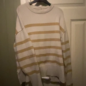 Randig beige och vit stickad tröja - Mysig stickad tröja med breda beige och vita ränder. Tröjan har en rund halsringning med ribbad kant och långa ärmar. Perfekt till vinter och höst