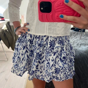 Vit och blå mönstrad kjol Gina Tricot - Supersöt kort kjol från Gina Tricot i vitt med blått blommigt mönster. Kjolen har volanger och resår i midjan, så fin för sommaren!!❤️👏👏👏