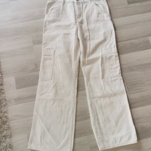 Cremvita cargo jeans från H&M, strl 44 - Snygga vita cargo jeans från H&M i storlek 44. Byxorna har raka ben, stora fickor på sidorna och är tillverkade i bomull. Perfekta för en avslappnad och trendig look. Passar dig som gillar loose fit och streetstyle. Endast provade. 