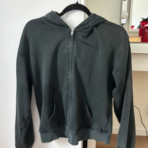 Mörkgrå hoodie med dragkedja - Enkel och stilren mörkgrå hoodie med dragkedja framtill och huva. Tröjan har långa ärmar och två fickor vid magen. Använd med i bra skick! Inga skador eller liknande