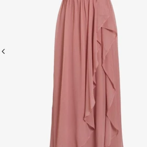 Lång rosa omlottklänning med volang - Superfin långklänning i en mjuk rosa nyans med omlottliv och v-ringning. Klänningen har korta, luftiga ärmar och snygga volangdetaljer framtill. Perfekt flowy passform och tillverkad i ett lätt polyestertyg som ger en skön känsla.