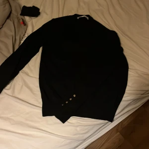 Svart stickad tröja från Zara med knappar - Svart stickad tröja från Zara i storlek M. Tröjan har lång ärm och snygga silvriga knappar vid ärmsluten som ger en stilren touch. Perfekt för dig som gillar enkel men trendig stil.