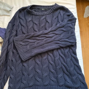 Mörkblå kabelstickad tröja Gina Tricot - Kabelstickad mörkblå tröja från Gina Tricot med grovt mönster och rund hals. Tröjan har långa ärmar och ribbade muddar vid ärmslut och nederkant. Storlek M men passar även L väldigt stor i storlek