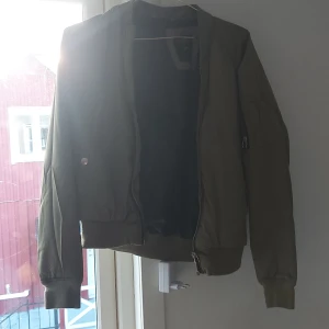 Olivgrön bomberjacka XS Black Label - Snygg olivgrön bomberjacka från The Black Label Collection i storlek XS. Jackan har klassisk bomberstil med ribbade muddar, dragkedja framtill och ficka med dragkedja på ärmen. Perfekt för dig som vill ha en stilren och trendig look.