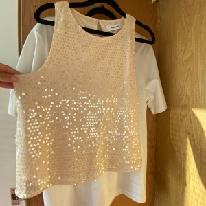Champagnefärgad paljettopp Kappahl - Säljer en champagnefärgad ärmlös topp från Kappahl, täckt med glittrande paljetter. Toppen har rund halsringning och en lätt A-linjeformad passning. Perfekt för dig som vill sticka ut med lite extra bling.