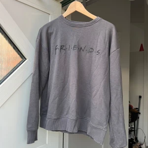 Grå FRIENDS sweatshirt från NA-KD - Grå sweatshirt från NA-KD med FRIENDS-tryck framtill. Tröjan har rund hals, ribbade muddar och avslappnad passform. Perfekt för dig som älskar tv-serien och vill ha en chill och snygg look. Tillverkad i mjuk bomull. Mycket sparsamt använd! Vill få den såld så därav priset som även går att diskutera🥰🥰