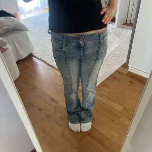 Blå bootcut jeans från Bershka - Snygga ljusblå bootcut jeans från Bershka med markerade sömmar längs benen och dubbla knappar i midjan. Jeansen är tillverkade i bomull med lite stretch för extra komfort. 🩵