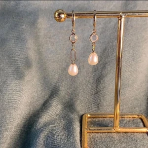 Guldörhängen med pärldroppar - Snygga örhängen i guldton med hängande vita pärldroppar och en rund kristall ovanför. De har en elegant och stilren design med små länkar mellan kristallen och pärlan. Perfekta för att lyfta din look med en touch av lyx.