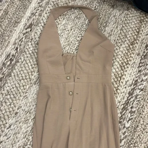 Beige jumpsuit med knappar - Snygg beige jumpsuit med halterneck och knappar framtill. Storlek XS från SHEIN