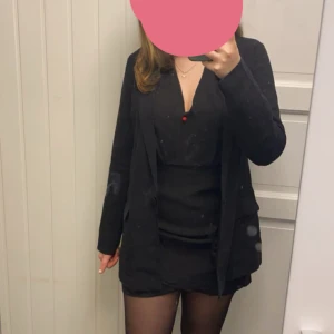 Svart klänning - Säljer en svart kort klänning med v-ringning och omlottkänsla. Klänningen har långa, transparenta ärmar och dragkedja i ryggen. Snygg och stilren modell som passar perfekt till dig som gillar en enkel men elegant look.  Storlek M men passar mer S