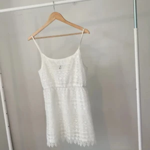 Vit spetsklänning från H&M Divided - Superfin vit kortklänning från H&M Divided med tunna axelband och vacker spets över hela klänningen. Klänningen har blommigt spetsmönster, rak passform och fodrad insida. Perfekt för sommarens alla tillfällen!