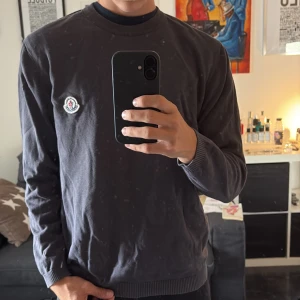 Svart Moncler sweatshirt i bomull - Svart sweatshirt från Moncler med klassisk rund hals och broderad logga på bröstet. Tröjan har ribbade muddar vid ärmslut och nederkant, och är tillverkad i mjuk bomull. Perfekt för dig som gillar stilrena och exklusiva plagg.