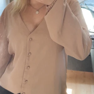 Beige Blus med knappar Even&Odd - Stilren beige Blus från Even&Odd med v-ringning och klädda knappar framtill. Mjuk känsla i tyget och enkel design som ger en clean look. Perfekt för dig som gillar minimalistiskt mode.