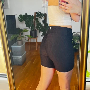 Svarta cykelbyxor från Guess - Säljer ett par svarta högmidjade cykelbyxor från Guess. De har en ribbad struktur och tight passform som framhäver formerna. Perfekta för träning eller när du vill ha en sportig look. Materialet är stretchigt och bekvämt.