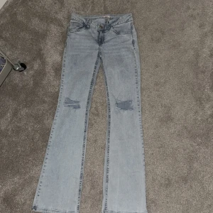 Ljusblå bootcut jeans från Nelly - Snygga ljusblå jeans från Nelly med bootcut passform och slitna detaljer vid knäna. Jeansen har klassisk femficksdesign, röda sömmar på bakfickorna och är tillverkade i mjukt denimtyg. Perfekta för dig som gillar en retro vibe och vill sticka ut lite extra.