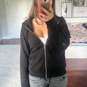 Svart hoodie med dragkedja från H&M Divided - Svart huvtröja från H&M Divided med dragkedja framtill, huva med snörning och två fickor. Tröjan är välanvänd men har inga synliga defekter (fläcken är på spegeln). Säljer tröjan pga att den aldrig används längre💕