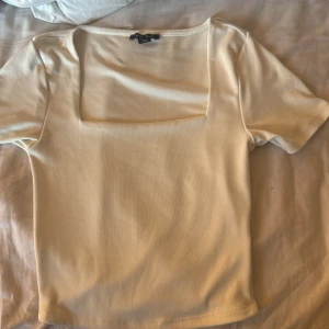 Vit topp med fyrkantig ringning Amisu - Snygg vit topp från Amisu med korta ärmar och trendig fyrkantig ringning. Modellen är figurnära och passar perfekt till jeans eller kjol. Mjuk och stretchig bomullsblandning som känns skön mot huden.