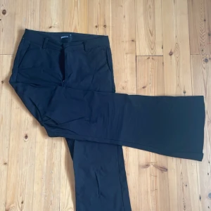 Svarta kostymbyxor från Gina Tricot - Riktigt snygga, svarta kostymbyxor från Gina Tricot i flare/bootcut modell. Byxorna har hällor för bälte, snedställda fickor fram och en dekorativ ficka bak. Perfekta för en clean och stilren look. Använda några gånger men blev för små, därav nytt skick efter en strykning då dom är lite skrövliga❤️