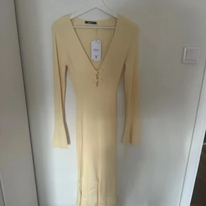 Lång ljus ribbad klänning från NA-KD - Superfin långklänning i ljus beige ton från NA-KD. Klänningen är ribbad, har långärmade trumpetärmar och djup v-ringning med snygga snörningsdetaljer framtill. Materialet är mjukt och stretchigt, perfekt för dig som gillar en slim passform.