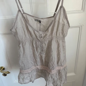 Linne från Hunkydory - Supersöt linnetopp från Hunkydory med smala axelband, v-ringning och knappar framtill. Toppen har en volangkant nertill och spetsdetaljer. 