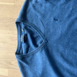 Blå v-ringad tröja Polo Ralph Lauren - Snygg blå v-ringad tröja från Polo Ralph Lauren i mjuk pima bomull. Klassisk design med diskret broderad logga på bröstet och ribbade muddar vid ärmslut och nederkant. Perfekt för dig som gillar stilrena och tidlösa plagg.
