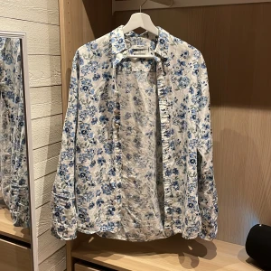 Blommig vit skjorta från Jack & Jones - Snygg vit skjorta från Jack & Jones med blått blommigt mönster. Slim fit-modell med långa ärmar och klassisk krage. Tillverkad i mjuk bomull, perfekt för dig som gillar att sticka ut med stilrena detaljer och fräscha färger. Knappar framtill och på manschetterna.