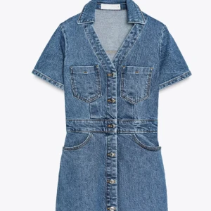 Blå jeansklänning med knappar - Säljer en kort jeansklänning i klassisk blå denim med korta ärmar och v-ringad krage. Klänningen har framfickor på bröstet och höften samt snygga metallknappar hela vägen framtill.
