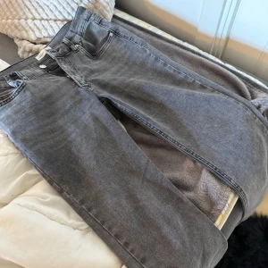 Grå bootcut jeans med låg midja - Säljer ett par grå jeans med bootcut-modell och låg midja. Jeansen har klassisk femficksdesign, raka ben som blir vidare nedtill och stängs med knapp och dragkedja  och har en snygg tvättad grå färg men alldeles för stora för mig. 