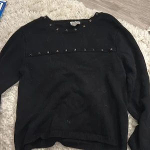 Svart stickad tröja med nitar från hm - Svart stickad tröja från DIVIDED i storlek XS. Tröjan har långa ärmar och coola silverfärgade nitar längs halsringningen och bröstet. Ribbad kant vid hals, ärmslut och nederkant. Perfekt för dig som gillar edgy detaljer och enkel stil.