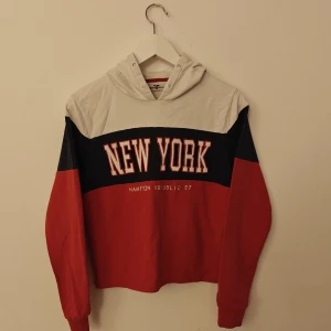 Hampton Republic hoodie - Säljer en snygg hoodie från Hampton Republic med coolt New York-tryck. Tröjan har färgblock i vitt, marinblått och rött, huva och långa ärmar. Tillverkad i 100% bomull, perfekt för dig som gillar streetstyle och vill sticka ut.