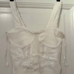 Vit korsett-topp med spets från Zara - Supersöt vit ribbad korsett-topp från Zara. Toppen har broderade spetsdetaljer och blommiga applikationer framtill. Sååå himla fin till vår/sommar. 🌞Helt nyköpt och därmed oanvänd, med prislappen kvar (se bilder). Säljer då den inte passar!! 💖💖Bara att skriva om eventuella frågor uppstår, eller om du vill ha fler bilder!☀️🩷