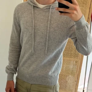 Grå hoodie med huva och snörning storlek xs - Säljer en stilren grå hoodie med huva och snörning. Tröjan har långärmade ribbade muddar och är gjord i mjukt stickat material som känns skönt mot huden. Perfekt för chill dagar och enkel att matcha med jeans eller joggers.