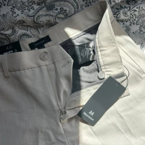 Offwhite kostymbyxor från Matinique - Snygga offwhite melange kostymbyxor från Matinique, modell MAliam Pant. Byxorna har klassisk passform, bälteshällor, knäppning med dragkedja och knapp samt två bakfickor med knapp. Perfekta för en clean och stilren look.