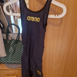 Arena Tävlingsbaddräkt - Modell: Flex, grå färg med svart baksida, guld detaljer, FINA märkt, öppen rygg