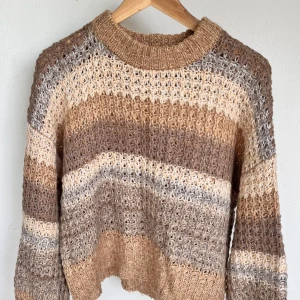 Randig stickad tröja i beige och brunt - Supermysig stickad tröja med breda ränder i beige, brunt och grått. Tröjan har en chunky känsla med grovstickad struktur och ribbad hals, ärmslut och nederkant. Perfekt för dig som gillar chill och avslappnad stil. Liten i storleken, skulle säga att den sitter mer som en S