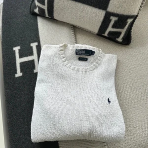 Vit stickad tröja från Polo Ralph Lauren - Vit stickad tröja från Polo Ralph Lauren i 100% bomull. Klassisk rund halsringning, ribbade muddar och diskret broderad logga på bröstet. Perfekt för en clean och stilren look. ÄR ÖPPEN FÖR TRADE OCKSÅ!
