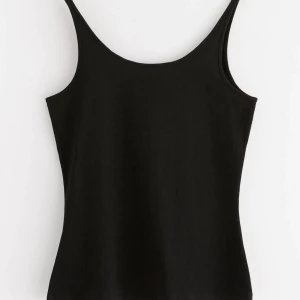 Svart linnetopp från Lindex - Svart, stilren linnetopp från Lindex med smala axelband och rundad halsringning. Toppen är figurnära och tillverkad i mjuk bomull som känns skön mot huden. Perfekt att matcha med jeans eller kjol för en enkel och snygg look.