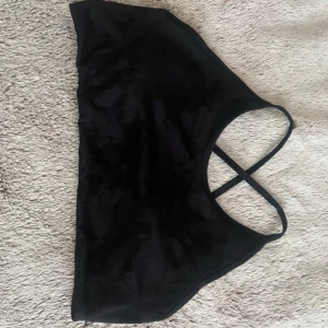 Svart sport-bh från Relode - Säljer en svart sport bh från Relode med tunna korsade axelband i ryggen. Toppen är i ett stretchigt material som passar perfekt till träning. Enkel och stilren design med liten logga på sidan. Perfekt för dig som gillar sportiga och bekväma plagg. Nypris 499