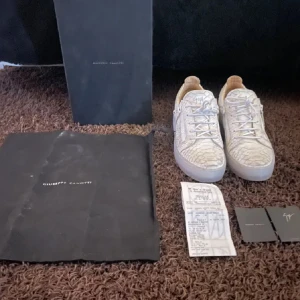 Giuseppe Zanotti vita sneakers med färgstänk - Unika vita sneakers från Giuseppe Zanotti med coolt färgstänkt mönster i rosa, blått och gult. Skorna har snörning, dragkedjor på sidorna och en texturerad yta som påminner om ormskinn. Perfekta för dig som vill sticka ut med din stil.