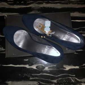 Mörkblå mocka pumps från Jana - Snygga mörkblå pumps från Jana i mjuk mocka med rund tå och stabil klack. Skorna har en klassisk siluett och är perfekta för dig som gillar stilren design med lite extra komfort. Innersulan är silverfärgad och skon har en låg klack som ger bra stöd.