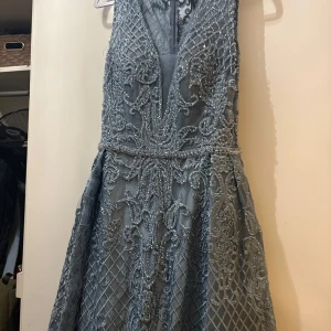 Blå långklänning med paljetter - Säljer en blå långklänning med djup v-ringning och detaljerad broderad spets samt glittriga paljetter över hela klänningen. Klänningen har ett elegant mönster och är ärmlös, perfekt för bal eller fest. Materialet känns lyxigt och skimrande.