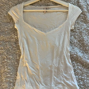 Vit v-ringad topp med spetskant - Vit T-shirt med spets kant runt v-ringningen från Nelly, använd ett fåtal gånger. Skriv om du skulle önska fler bilder😁😁