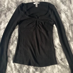 Svart tröja - Svart ribbad långärmad topp från H&M i storlek XS. Toppen har en snygg v-ringning med snörningsdetalj framtill och figurnära passform. Materialet är stretchigt och bekvämt, perfekt till jeans eller kjol.
