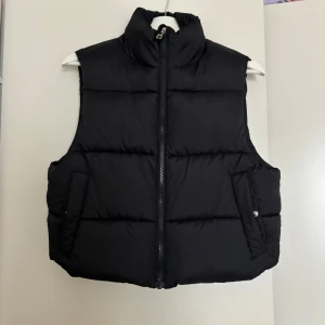 Svart dunväst från Lager 157, storlek S - Säljer en svart, quiltad dunväst från Laget 157 i storlek S. Västen har hög krage, två fickor med tryckknapp och dragkedja framtill. Perfekt att slänga över en hoodie för en cool och avslappnad look.