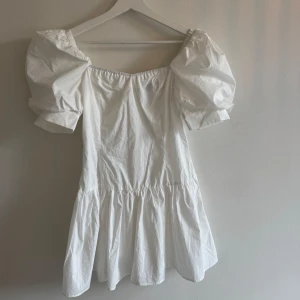 Vit kort klänning med puffärmar  - Supersöt vit klänning med puffiga korta ärmar och volang nedtill som aldrig kommit till användning. Puffärm och volang. Har dragkedja i ryggen. Jag har massor av artiklar till salu! Köp flera och få rabatt!Modellen har en fyrkantig urringning och är tillverkad i lätt bomullstyg. Perfekt för dig som gillar romantisk och trendig stil med lite extra volym på axlarna.