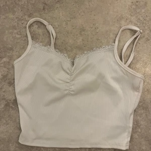 Vit ribbad linnetopp från SHEIN XS - Supersöt vit ribbad linnetopp från SHEIN i storlek XS. Toppen har smala justerbara axelband, spetskant upptill och en snygg rynkdetalj vid bysten. Perfekt för varma dagar eller att styla lager på lager.