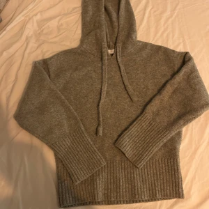 Grå stickad hoodie från Zara - Mysig grå hoodie från Zara i stickat material med huva och snörning. Tröjan har breda ribbade muddar vid ärmslut och nederkant, samt lång ärm. Perfekt för kalla dagar när du vill vara både chill,snygg och passar perfekt för hösten som kommer nu.