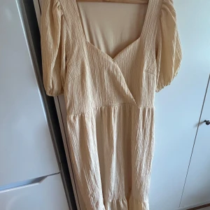  klänning från Nelly - Säljer en  klänning från Nelly med puffiga korta ärmar och v-ringad omlottfront. Klänningen har en lätt rynkad struktur i tyget och ett flowy fall. 