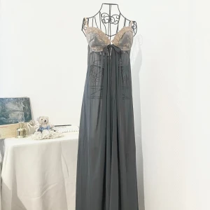 Grå nattlinne från Victoria’s Secret - En grå nattlinne från Victoria’s Secret med en slits framtill och guld spetsdetaljer. Ganska genomskinlig och lång (täcker hela fötter om du är kortare än 160cm). Storlek: XL (42), passar även storlek L om du har stor byst. Byst: över 100cm. Dockans storlek: 34.